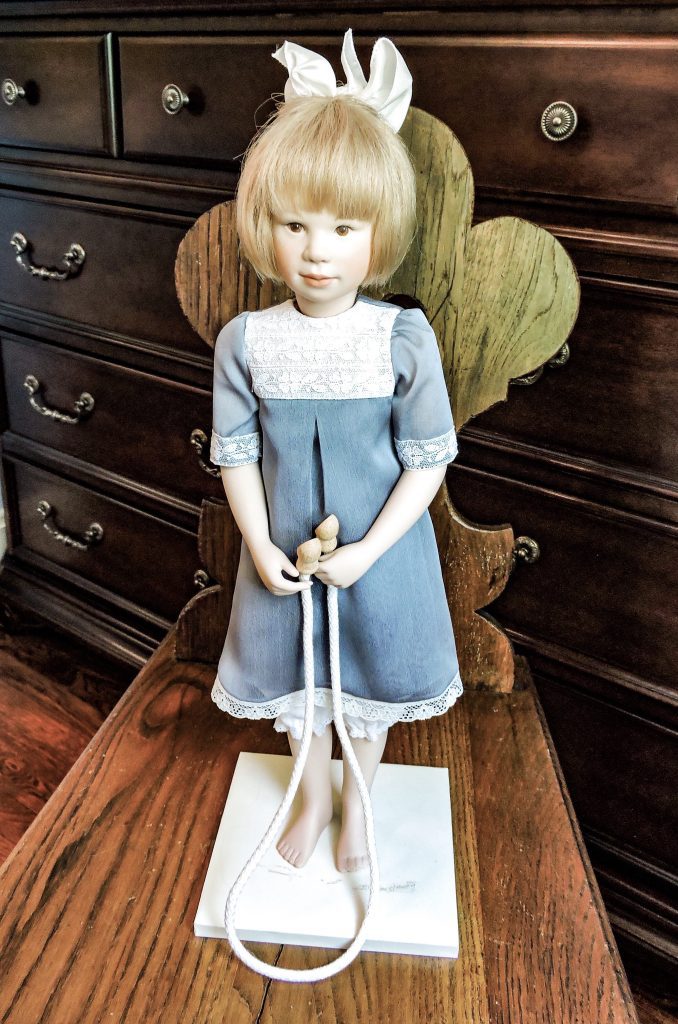 A highly detailed image of a Francoise doll, featuring a bisque porcelain body with human hair, dressed in a silk and lace outfit, and standing against a blurred background.