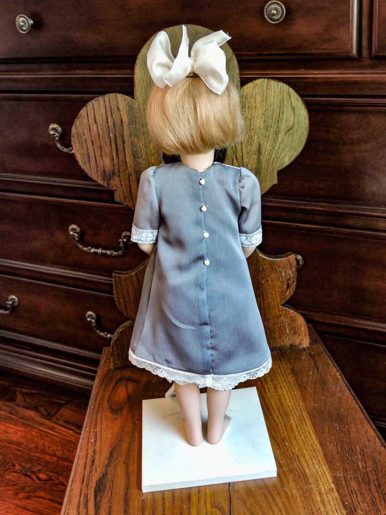 A highly detailed image of a Francoise doll, featuring a bisque porcelain body with human hair, dressed in a silk and lace outfit, and standing against a blurred background.