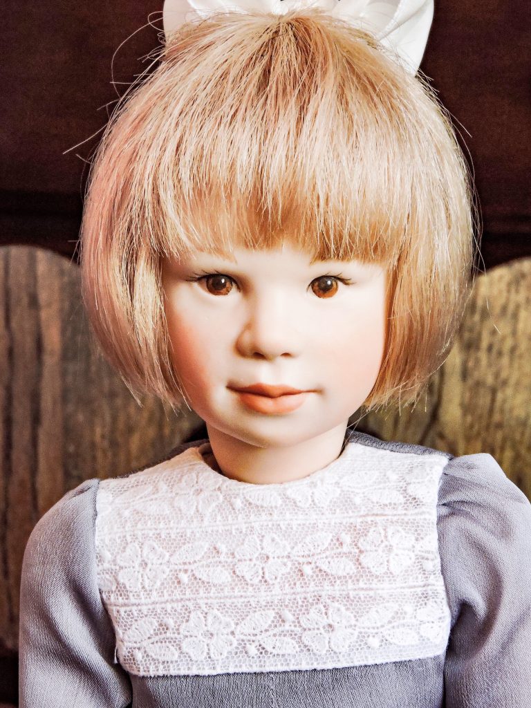 A highly detailed image of a Francoise doll, featuring a bisque porcelain body with human hair, dressed in a silk and lace outfit, and standing against a blurred background.