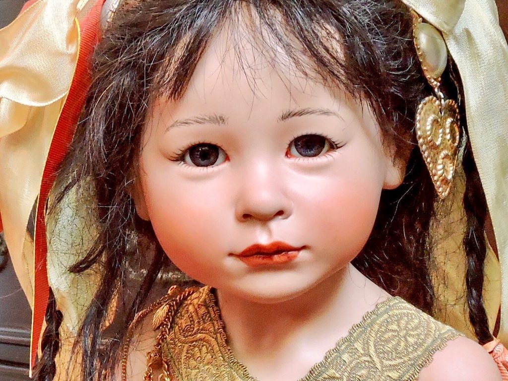 A porcelain doll with a red silk dress and leather sandals, holding a black bamboo umbrella, with a decorative floral hairpin and glass eyes.