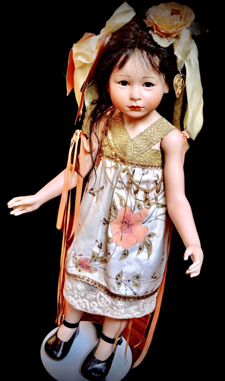 A highly detailed image of a Sakia porcelain doll, featuring a human hair wig, glass eyes, and a silk outfit with a red and gold belt. The doll has a realistic appearance with a natural bamboo umbrella.